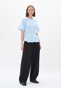 Světle modrý top s krátkými rukávy a peplum spodním lemem; spárován s černými širokými kalhotami a černými botami na slip.