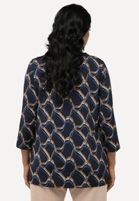 Marineblus med ett geometriskt mönster i beige och blått. Tillverkad av ett mjukt tyg, med trekvartslånga ärmar och en avslappnad passform.