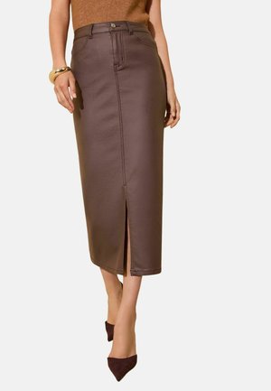 Mujer con falda midi de cuero marrón de talle alto con abertura frontal, top marrón, pulsera dorada y tacones marrones de punta afilada.