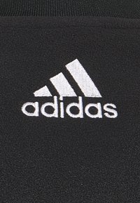 Schwarzer Fleece-Stoff mit einem weißen, gestickten Adidas-Logo und drei diagonalen Streifen über dem Namen, prominent präsentiert.