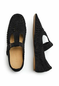 Bailarinas de ante negro con parte superior trenzada, lados abiertos y correa ajustable con hebilla. Suela plana de goma con sutil textura. Nombre de la marca "BALAGAN" visible en el interior.