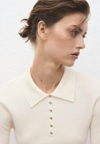 Pull en crème côtelé avec un col et une patte de boutonnage comportant des boutons métalliques. Texture lisse et coupe slim.