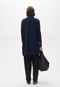 Camisa de manga larga azul marino oscuro con un ajuste relajado, combinada con pantalones negros holgados y un bolso tote negro texturizado. Diseño simple y moderno.