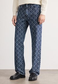 Jeans de denim azul con un patrón geométrico en azul claro, corte recto y diseño de cinco bolsillos. Cintura lisa con cierre de botón.