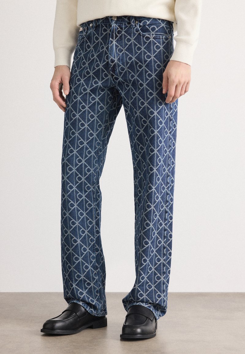 Jeans de denim azul con un patrón geométrico en azul claro, corte recto y diseño de cinco bolsillos. Cintura lisa con cierre de botón.