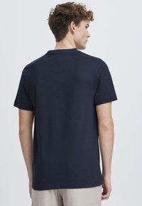 Marineblauwe katoenen t-shirt met korte mouwen en een ronde halslijn, met een minimalistisch ontwerp en subtiele stikdetails op de achterkant.