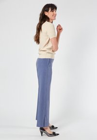 Beige knitted short-sleeve sweater paired with tailored light blue trousers featuring side slits, complemented by black pointed-toe heels with floral accents.