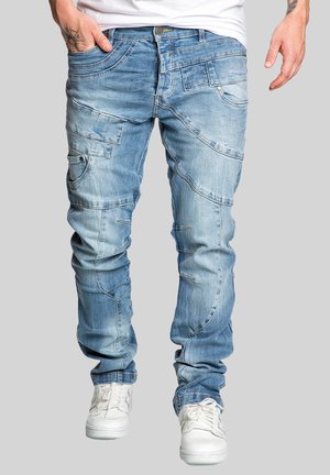 Light blue denim jeans featuring multiple pockets, visible stitching, and a tapered design, paired with white sneakers for contrast.