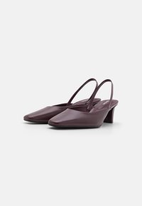 Burgundi bőr slingback sarkú cipők hegyes orral, vékony állítható pántokkal és közepes magasságú tömbsarkakkal. Simább textúra és minimalista design.