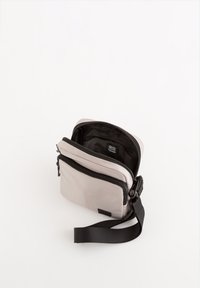 Svetle šedá crossbody taška s černým zipem a nastavitelným popruhem. Obsahuje jeden hlavní prostor a přední kapsu. Hladký povrch.