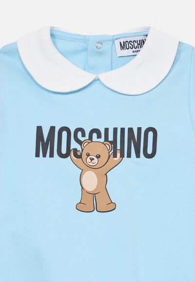 Light blue baby onesie with a white collar, featuring a print of a brown teddy bear and the text "MOSCHINO" in bold black letters.