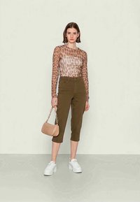 Blusa de mangas longas transparente com padrão de leopardo, combinada com calças cropped em verde-oliva. Acessórios incluem uma bolsa bege e ténis brancos.