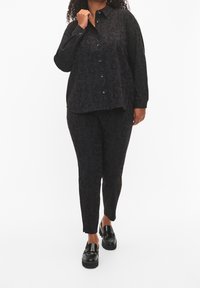 Svart blommönstrad blus med knäppning fram, ihopparad med matchande figurnära byxor. Båda plaggen har en subtil blomstertextur. Svarta loafers.