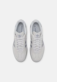 Šedé kožené tenisky se třemi šedými pruhy, kulatou špičkou, šněrovací konstrukcí a polstrovanou stélkou. Logo na jazyku a boku.