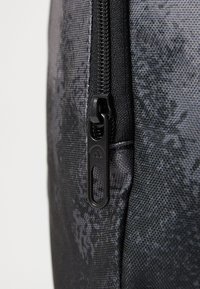 Čierny zips na šedej tkanine s jemnými vzormi vločiek, zobrazuje detailný záber zubov zipsu a šitia.