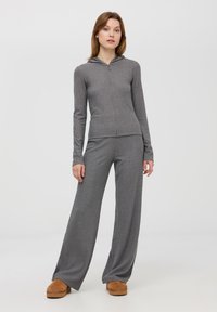 Szara, żebrowana bluza z kapturem z zapięciem na zamek i długimi rękawami, zestawiona z szerokimi, szarymi spodniami z żebrowanego materiału. Miękka tekstura i luźny krój.
