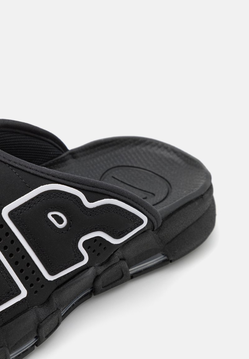 Sandalia deslizable negra con una suela de goma texturizada, correa ajustable y detalle de logo blanco con perforaciones en la parte superior para mayor transpirabilidad.
