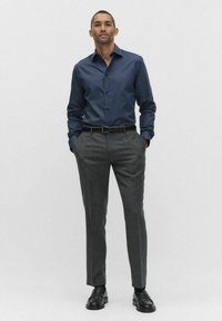 Granatowa, teksturowana koszula zapinana na guziki z długimi rękawami, zestawiona z dopasowanymi szarymi spodniami. Czarny pasek i mokasyny dopełniają strój.