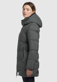 Giacca a vento grigia scura con cappuccio, caratterizzata da chiusura con zip e tasche laterali. Il materiale sembra morbido con una texture trapuntata.