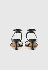 Sandales à talons noirs avec des brides de cheville étroites, des talons courbés et une finition en cuir lisse. Design ouvert mettant en valeur un style minimaliste.