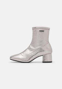 Botas de tobillo plateadas metálicas con punta afilada, caña corta, superficie texturizada y tacón cuadrado. Presentan costuras y un acento de logo.