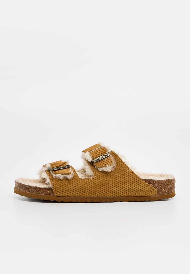 Braune Cord-Slidesandale mit zwei verstellbaren Schnallen und weißem Fleecefutter auf Korksohle.