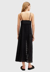 Black maxi dress with delicate lace detailing, adjustable thin straps, and a fitted bodice, flowing into a loose, ankle-length skirt.