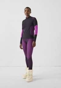 Top deportivo ajustado y leggings en negro y púrpura con rayas texturizadas. Modelo con botas color crema forradas de piel.