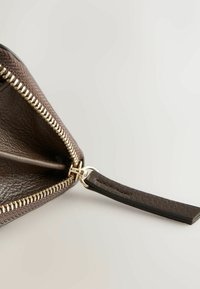 Sötétbarna bőr pénztárca cipzárral, arany színű fémrészletekkel és texturált felülettel. Kiváló minőségű bőrből készült varrott pánttal és belső rekesszel rendelkezik.