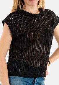 Top en maille noir à manches courtes, présentant un motif à mailles ouvertes, un col rond et une poche poitrine unique. Design texturé et léger.