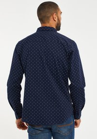 Marineblaues Hemd mit Knopfleiste, weißem Diamantmuster, langen Ärmeln und klassischem Kragen; aus glattem Stoff mit tailliertem Schnitt.