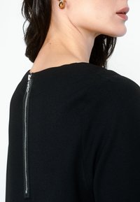 Abito nero con chiusura a zip sul retro, texture liscia e design semplice e sartoriale, con scollatura ampia e senza motivi visibili.