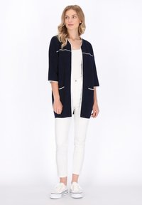 Cardigan navy con rifiniture bianche, apertura frontale e maniche a tre quarti. Abbinato a pantaloni bianchi slim-fit e sneakers bianche.