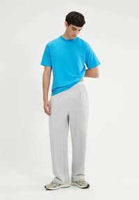 Camiseta corta de manga en color turquesa y pantalones de chándal grises claros. La camiseta tiene un escote redondo; los pantalones de chándal tienen un corte relajado y costuras laterales.