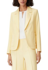 Yellow blazer made from smooth fabric, featuring a single button, two front pockets, and a notched lapel design. Paired with white top.