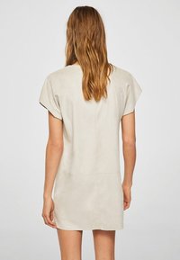 Krátké béžové šaty s hladkým povrchem a krátkými rukávy. Jednoduchý design má minimální švy a mírně volný střih.