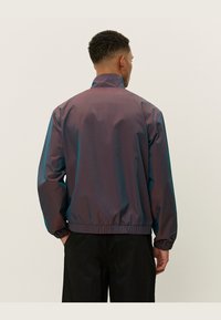 Vattentät jacka i ett gradient av lila och teal. Har elastiska ärmslut och fåll, med hög krage och en slät, glansig yta.