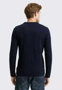 Marineblauwe trui met lange mouwen, geribbelde textuur en een ronde halslijn. De achterkant heeft minimale details en een gladde afwerking.