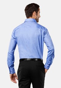 Camicia azzurra chiara a maniche lunghe con una texture liscia, colletto a punta e polsini abbottonati, abbinata a pantaloni neri e una cintura nera.