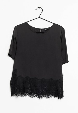 Blusa negra de manga corta con escote redondeado, colgando de una percha negra, con borde de encaje floral a lo largo del dobladillo inferior.