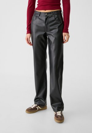 Person iført sorte læderbukser med lige ben, brune sneakers med hvide snørebånd og en cropped rød langærmet top.