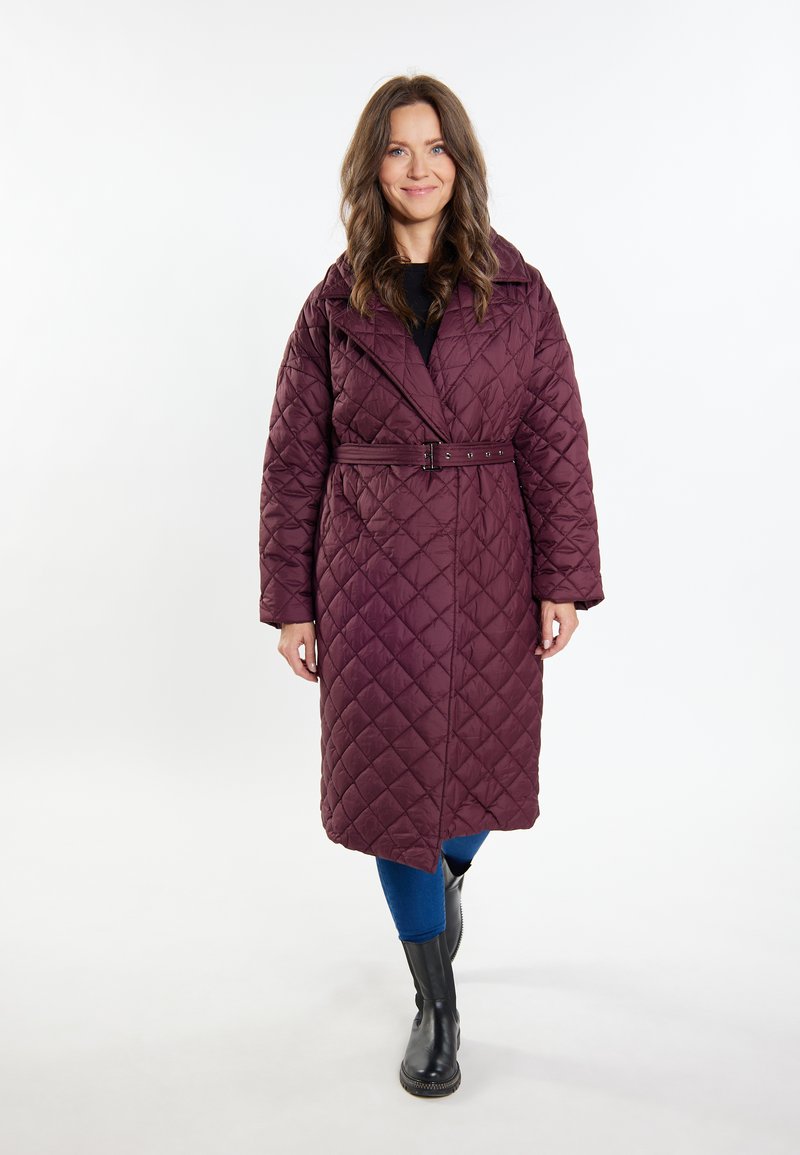 Cappotto bordeaux trapuntato con vita con cinturino, ampio colletto e maniche lunghe. Accompagnato da pantaloni blu e stivaletti neri.