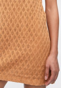 Adījuma kleita apdedzinātas apelsīna krāsā ar dimanta rakstu. Raksturīga vaļīga aušanas tekstūra un brīvs siluets. Beidzas virs ceļa.