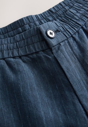 Pantaloni con vita elastica blu scuro, caratterizzati da una chiusura con bottone e sottili righe verticali su un tessuto strutturato.