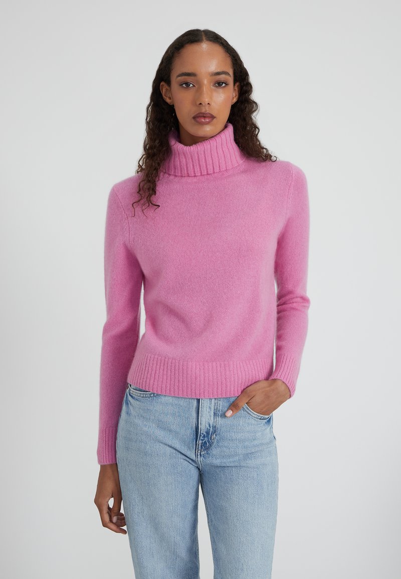 Maglione a collo alto in maglia fucsia con polsini e orlo a costine. Texture morbida e design aderente, abbinato a jeans a gamba dritta blu chiaro.