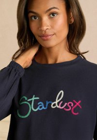 Marineblauwe sweatshirt met meerkleurige geborduurde tekst "Stardust". Zachte stof, lange mouwen met gathers aan de manchetten en een ronde halslijn.
