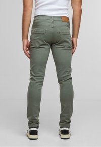 Olīvu zaļi slim-fit džinsi ar vidēju jostas līmeni, aizmugurējām kabatām un brūnu ādas uzlīmi uz vidusdaļas. Mīksta kokvilnas auduma maisījums.
