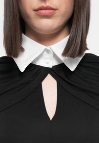 Schwarzes Kleid mit einem strukturierten weißen Kragen, ausgestattet mit einem Schlüssel-Ausschnitt und gerafften Stoffdetails an den Schultern.