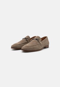 Suede loafers in a light brown color with a smooth finish, featuring a decorative silver hardware accent and a low-profile rubber sole.