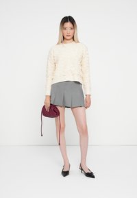 Maglione di collo alto in crema, gonna plissettata grigia, décolleté a punta nera e borsa a tracolla bordeaux. Outift moderno e semplice con dettagli sottili.
